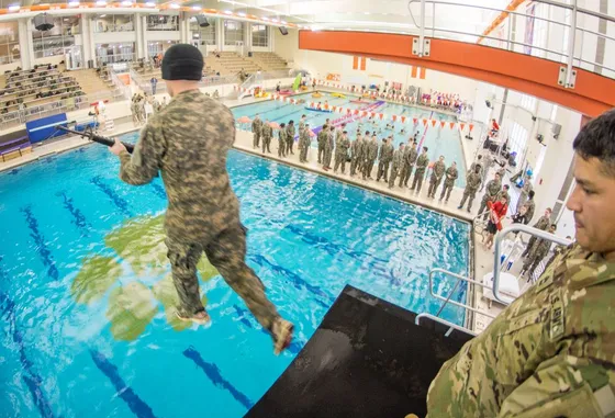 Army ROTC cadet leaping from the high-dive platform with a rifle during combat water survival training.