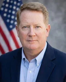 LTC Robert Kirkland, founder of ROTC Consulting, in a navy blazer in front of the American flag.