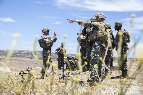A Marine instructor points downrange while cadets observe during live field training.