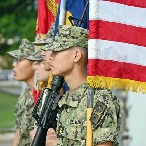 NROTC midshipmen color guard at attention with the American flag and unit colors.