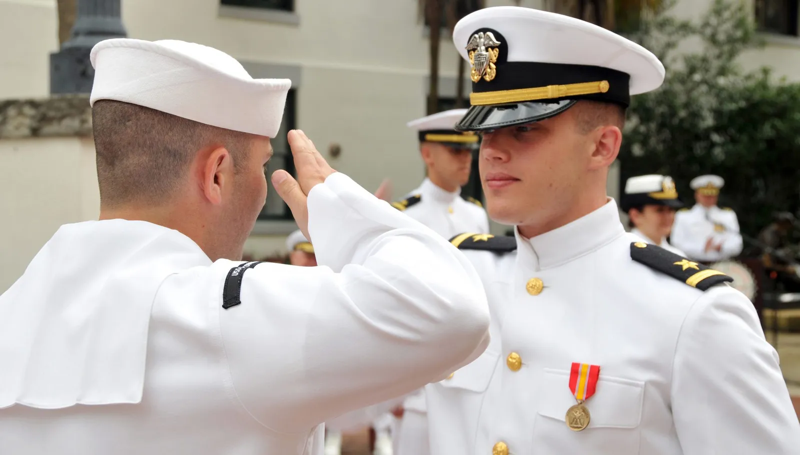 A newly commissioned Navy officer in dress whites receiving a first salute at a commissioning ceremony